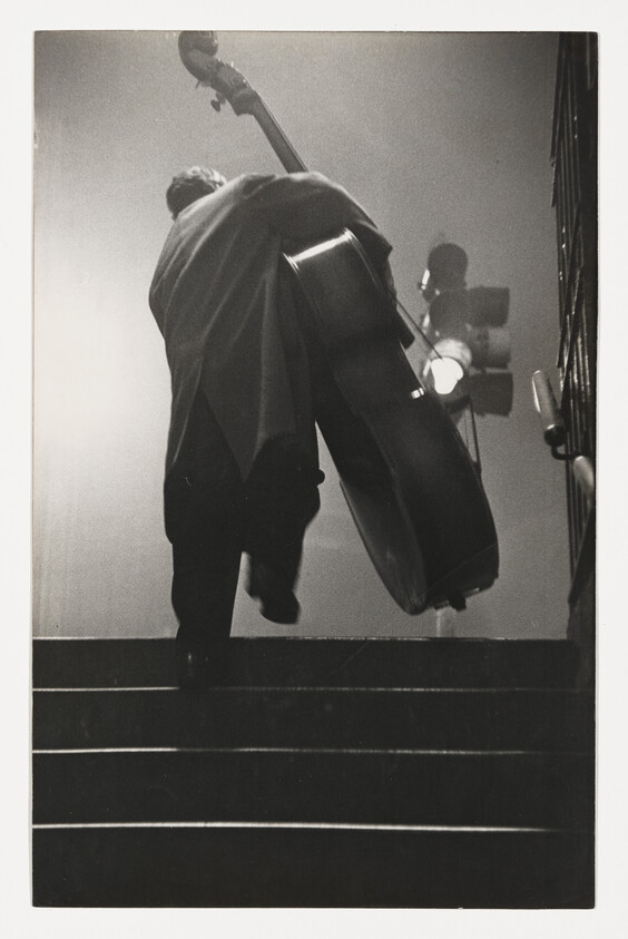 Person carrying a double bass up a staircase, with a traffic light visible in the background.