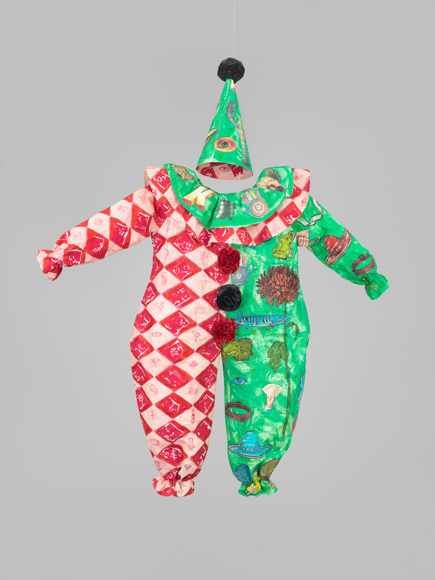 A colorful, patterned clown costume suspended in mid-air against a neutral background, featuring a conical hat with a pom-pom on top and a patchwork of different fabrics.