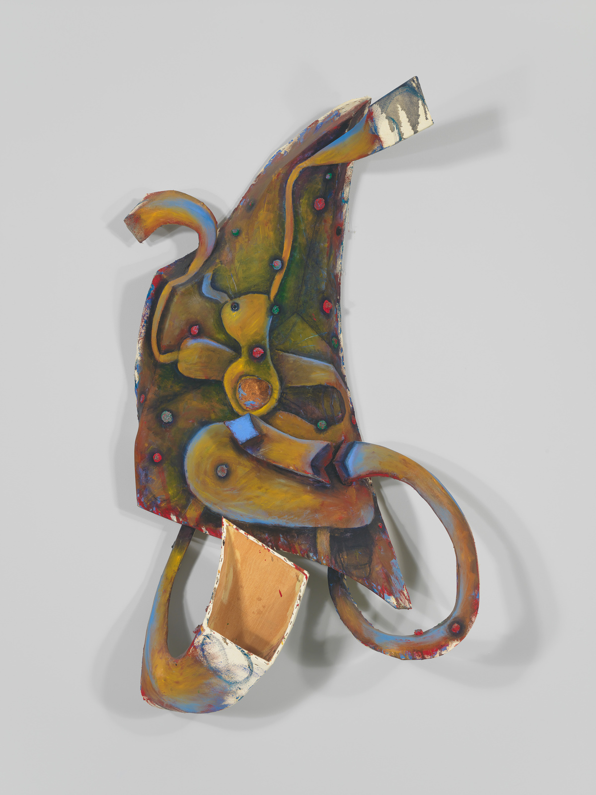 A colorful, abstract sculptural artwork mounted on a white wall, featuring organic shapes and a variety of textures, with elements that resemble loops and protrusions, painted in a palette of yellows, reds, blues, and earth tones.