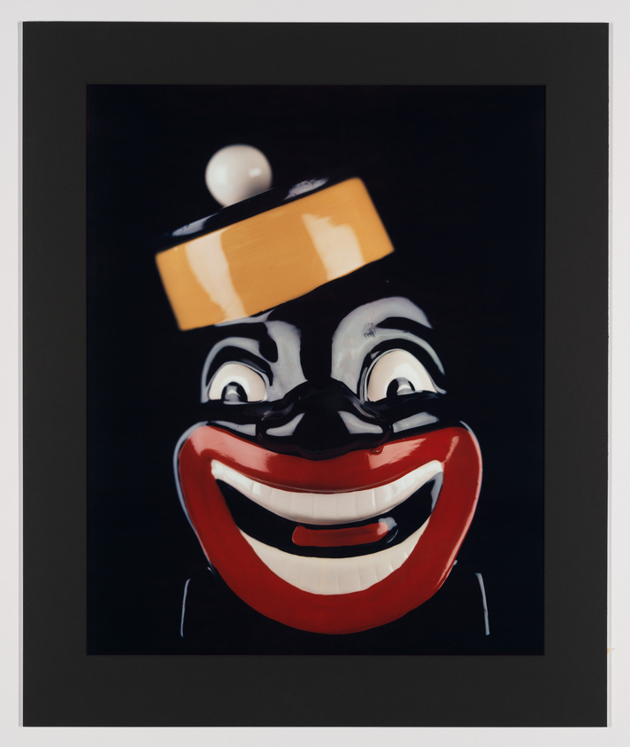 A stylized painting of a clown's face with exaggerated features, including a wide, red grin, black and white eyes, and a small hat with a ball on top, all set against a dark background and framed with a black border.