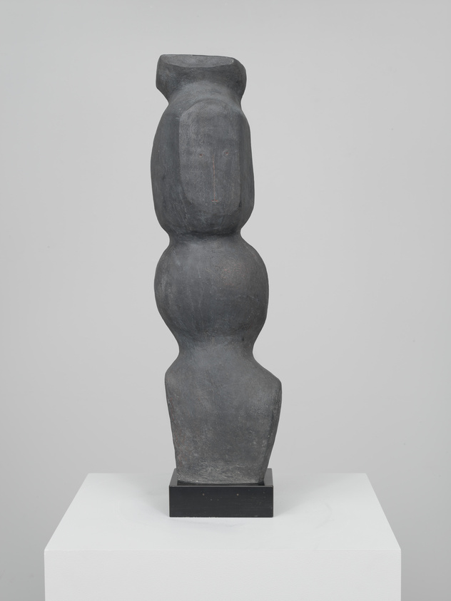 A tall, abstract stone sculpture with rounded shapes stands on a white pedestal.