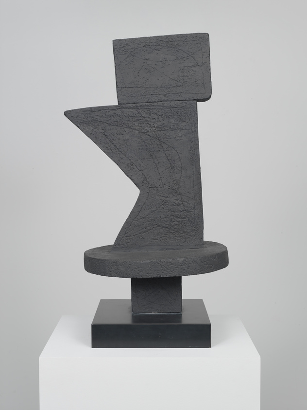 Abstract black sculpture with geometric shapes on a pedestal, featuring textured surfaces and angular design.