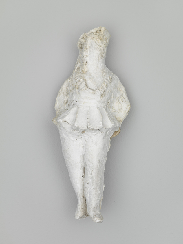 A white, textured sculpture of a female figure with no distinct facial features, mounted on a grey wall. The figure is depicted from the chest down to the knees, wearing a dress with a detailed bodice and a full skirt.