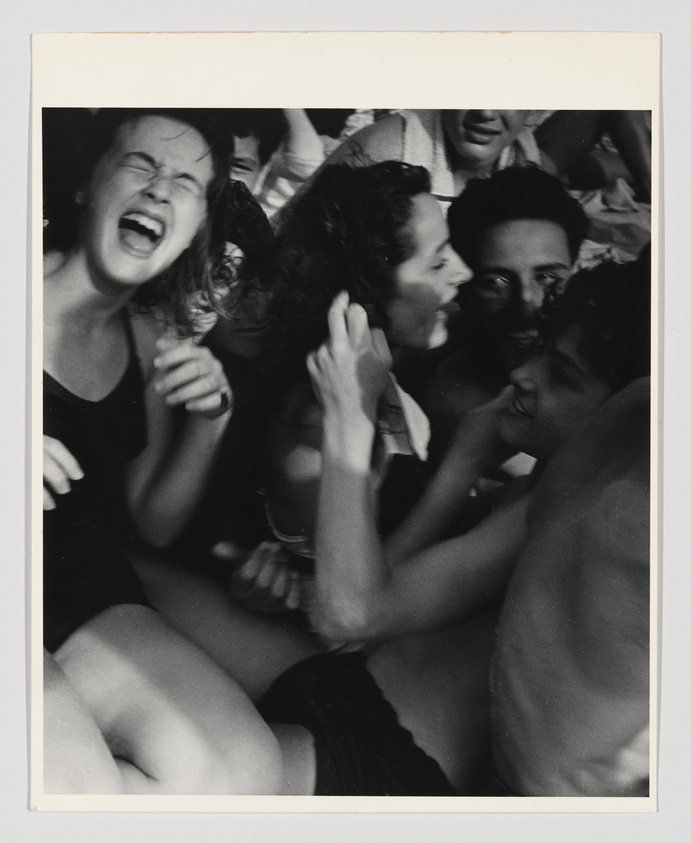 A black and white photograph capturing a group of people in a moment of intense emotion, with a young woman in the foreground screaming or cheering, her mouth wide open and eyes closed. She is surrounded by others who are also showing various expressions of excitement or enthusiasm.
