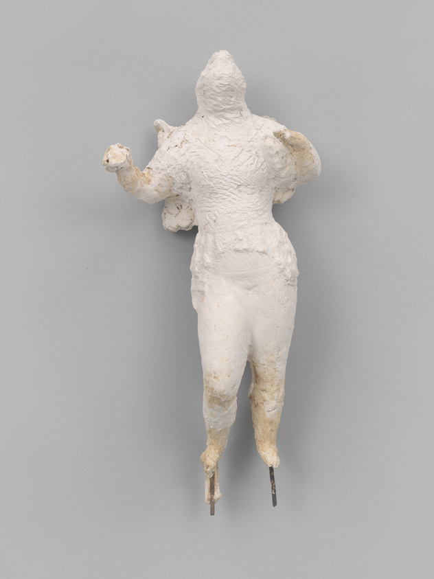 A textured white sculpture of a human figure without a defined head, arms outstretched, mounted on a gray background. The figure appears to be in motion, with one leg forward, and is supported by metal rods protruding from the feet.