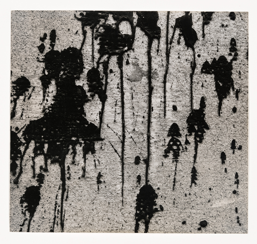 Black ink drips and splatters on a textured white background, creating an abstract composition.