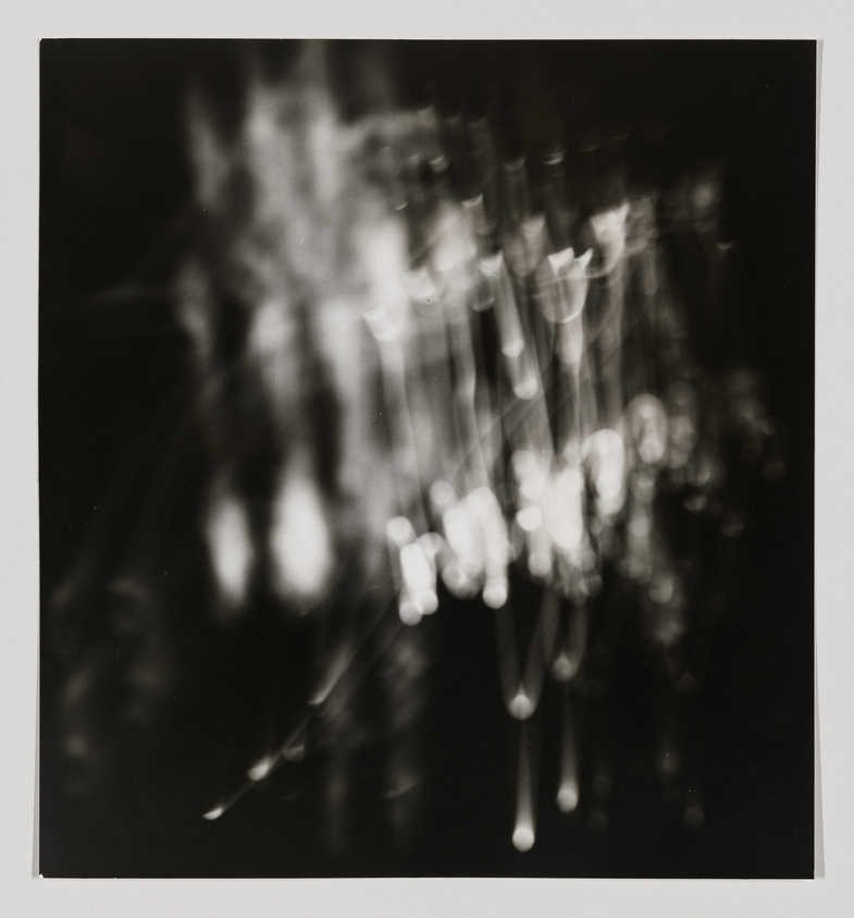 A black and white abstract photograph with blurred light patterns and streaks, creating a bokeh effect with a sense of motion or falling.