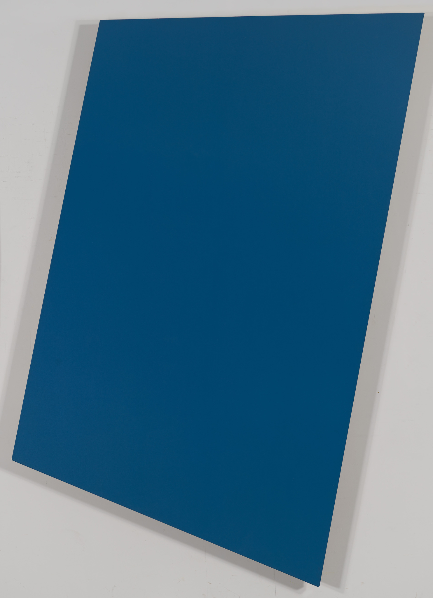 A large, solid blue canvas displayed at an angle against a white wall.