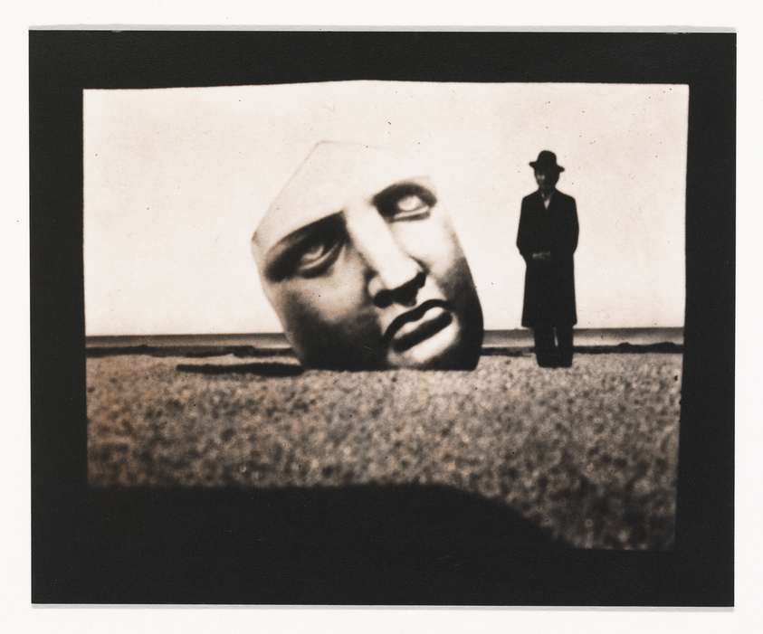 A surreal photo with a giant disembodied head on the ground and a small figure standing in the distance.
