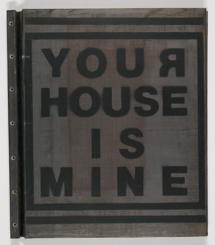 A stencil-like artwork with the phrase "YOUR HOUSE IS MINE" in bold, capitalized letters, reversed as if seen from behind the transparent surface it was painted on. The background appears metallic and shows signs of wear and aging.