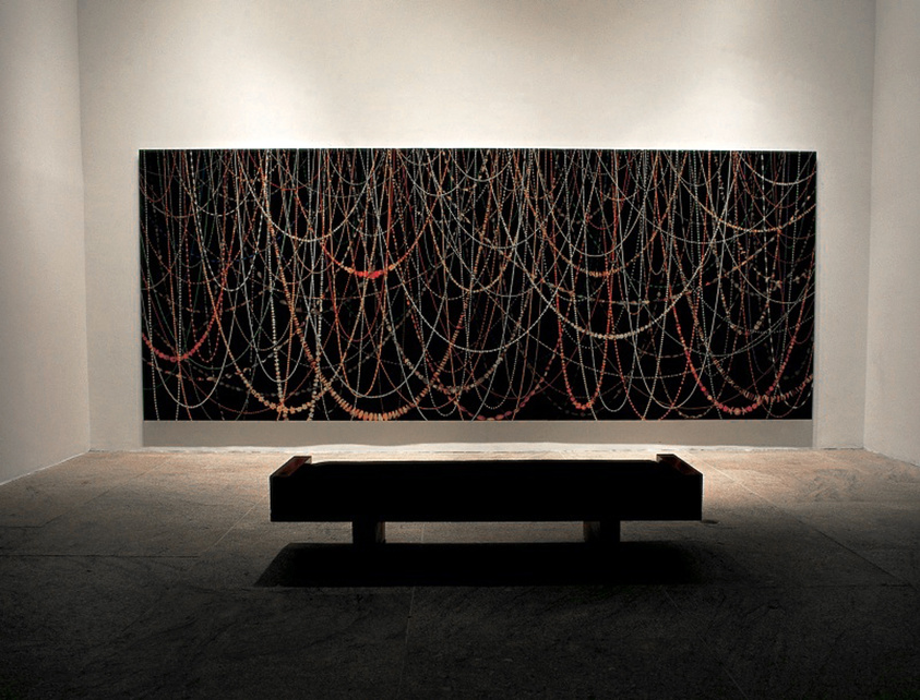 Large abstract painting with intersecting lines on a gallery wall, bench in front for viewing.