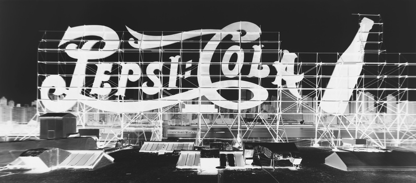 Black and white photo of a large, iconic Pepsi-Cola sign mounted on scaffolding.