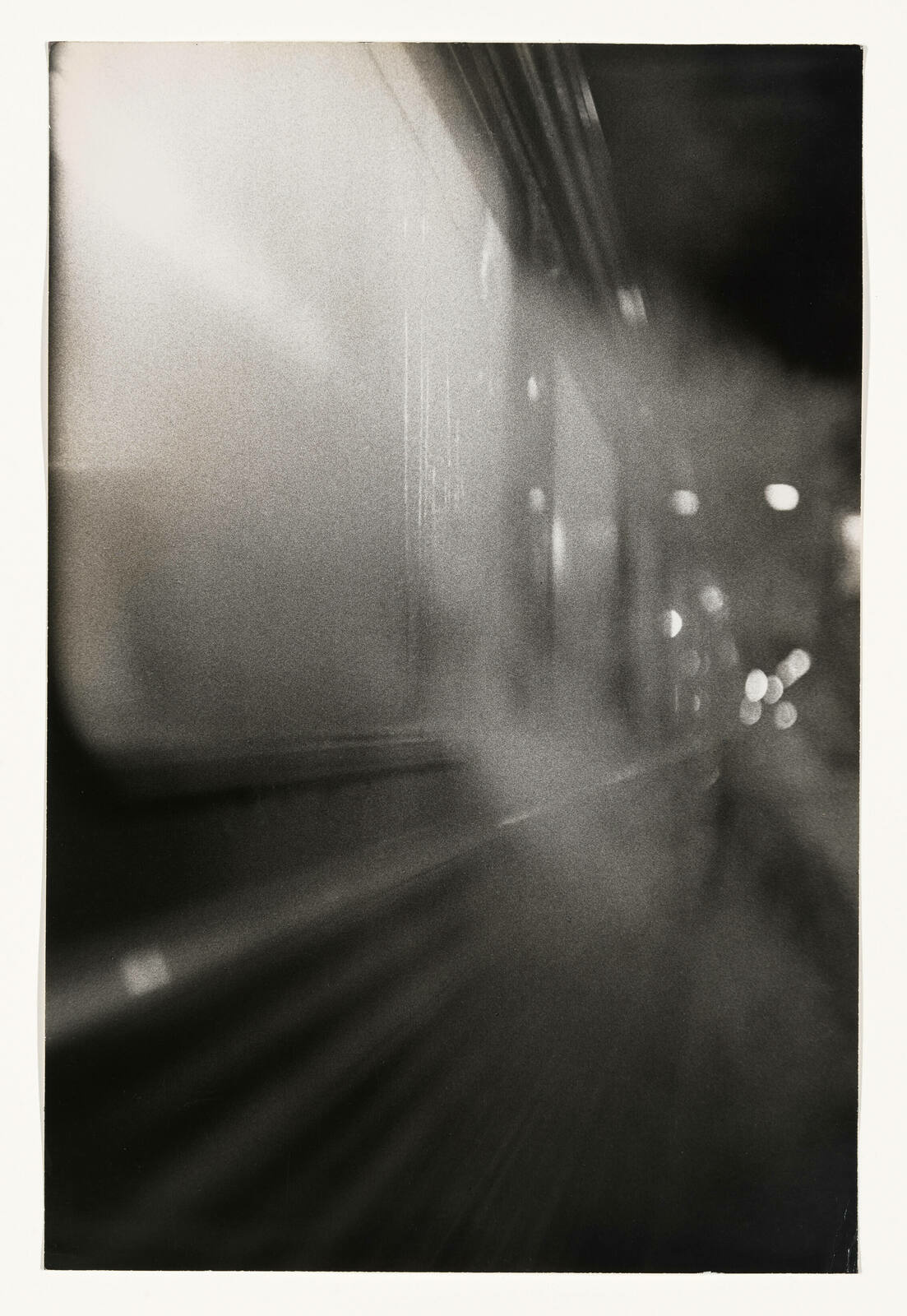 A black and white photograph capturing motion blur, likely from a moving train or subway, with light streaks and bokeh effects creating an abstract, dynamic scene.