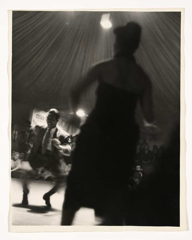 A man and a woman are dancing energetically in front of a crowd under a tent.