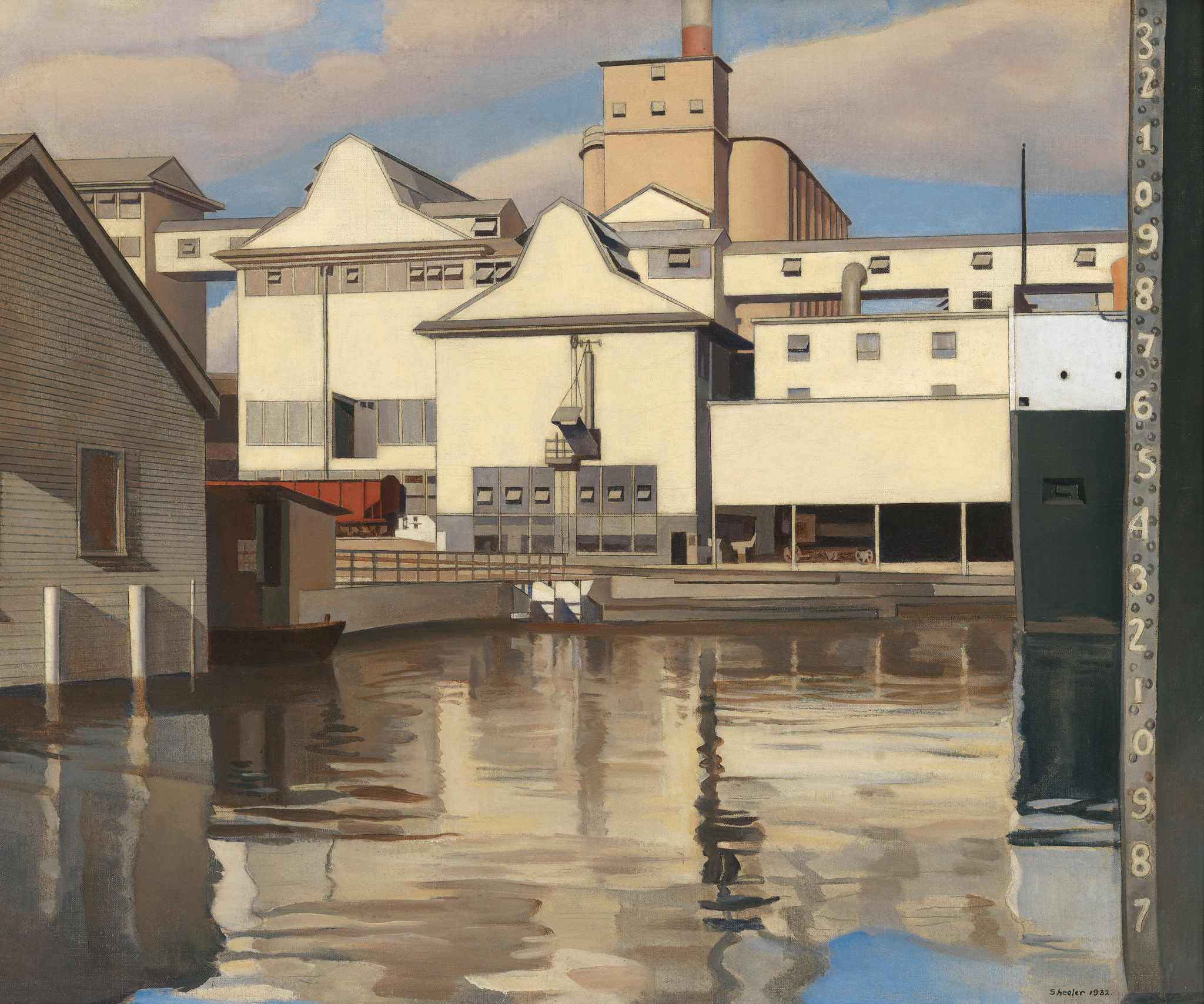 Industrial buildings by a waterfront with reflections in the water and a numbered gauge on the right.