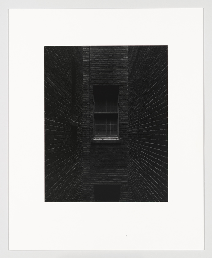 Black and white photo of a single window in a dark brick building shaft.
