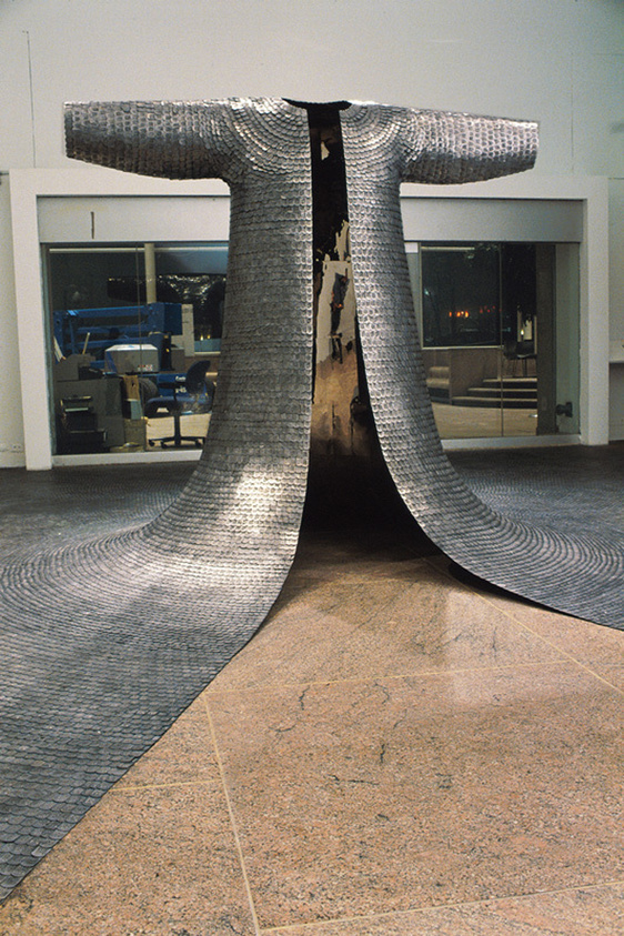 Sculpture resembling a split tree trunk with metallic bark texture, displayed indoors on a tiled floor.