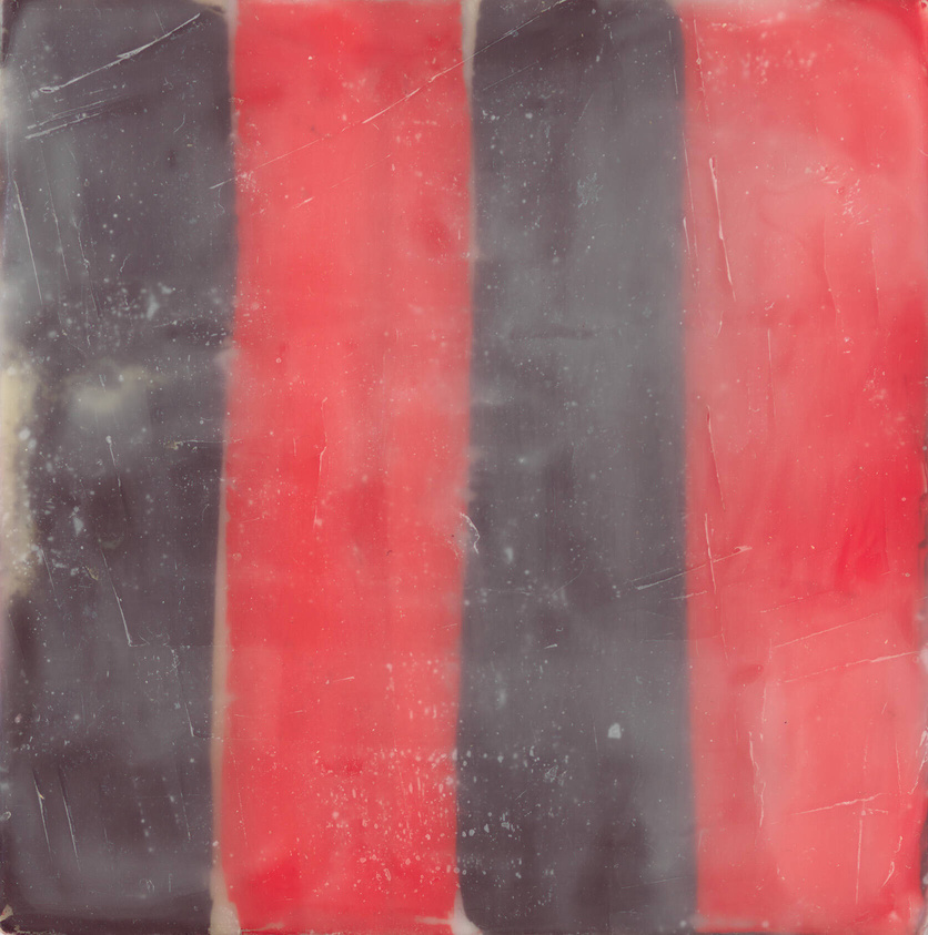 A close-up of a worn and scratched surface with vertical stripes in alternating colors of red and black.
