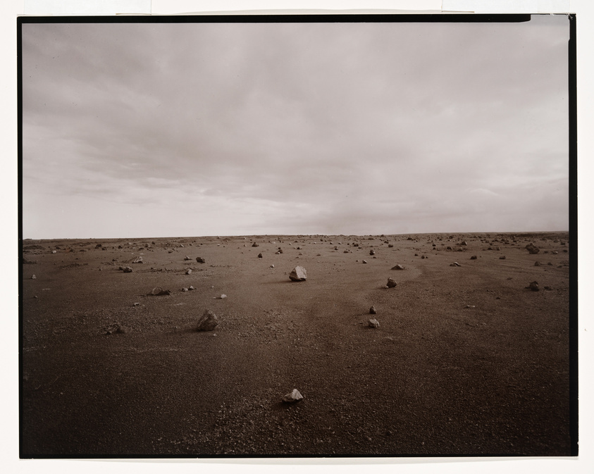 A sepia-toned photograph of a barren landscape scattered with rocks under a cloudy sky.