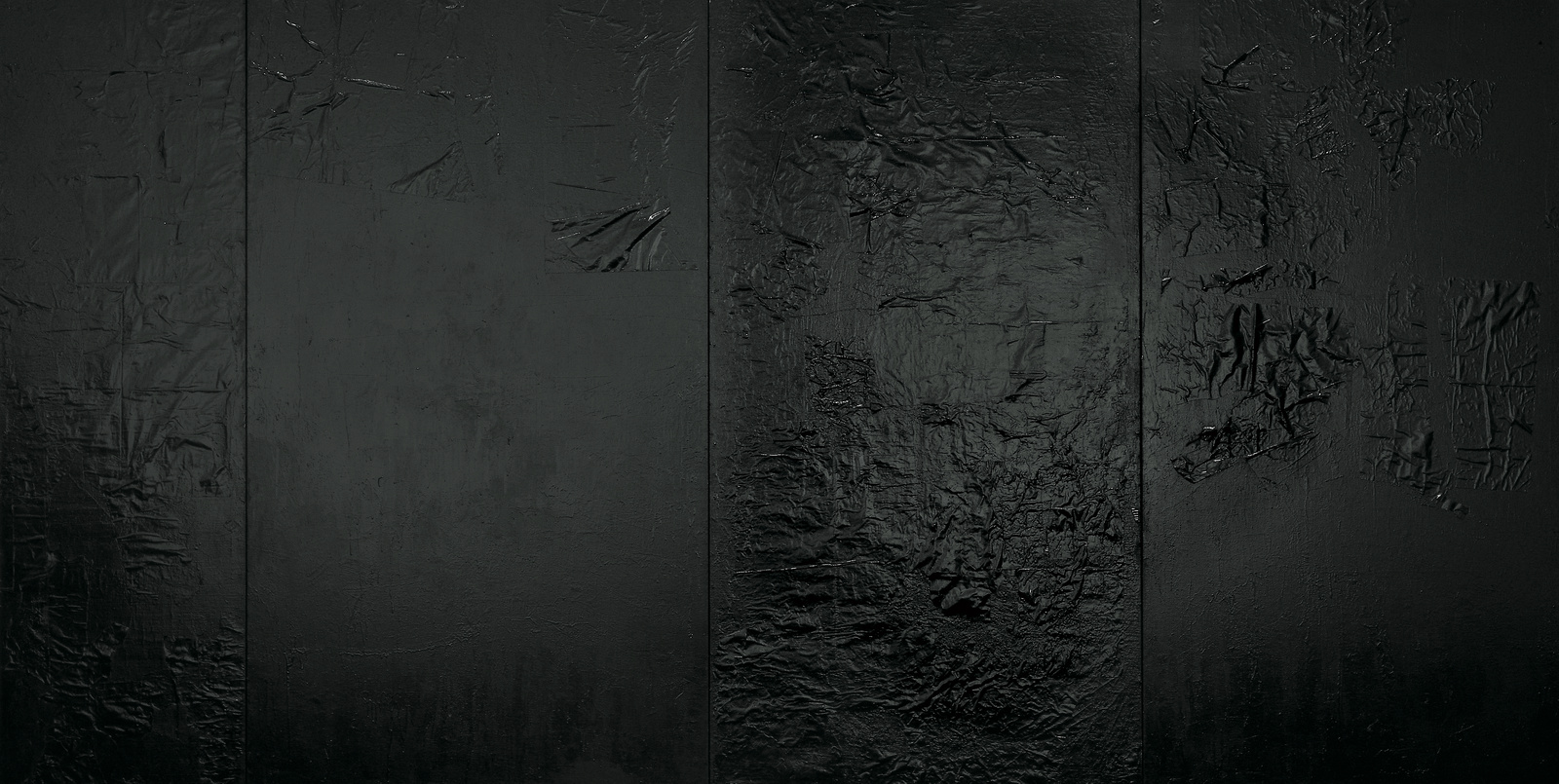 A dark, textured surface with various shades of black and gray, showing signs of wear and scratches, possibly a metal or painted wall.