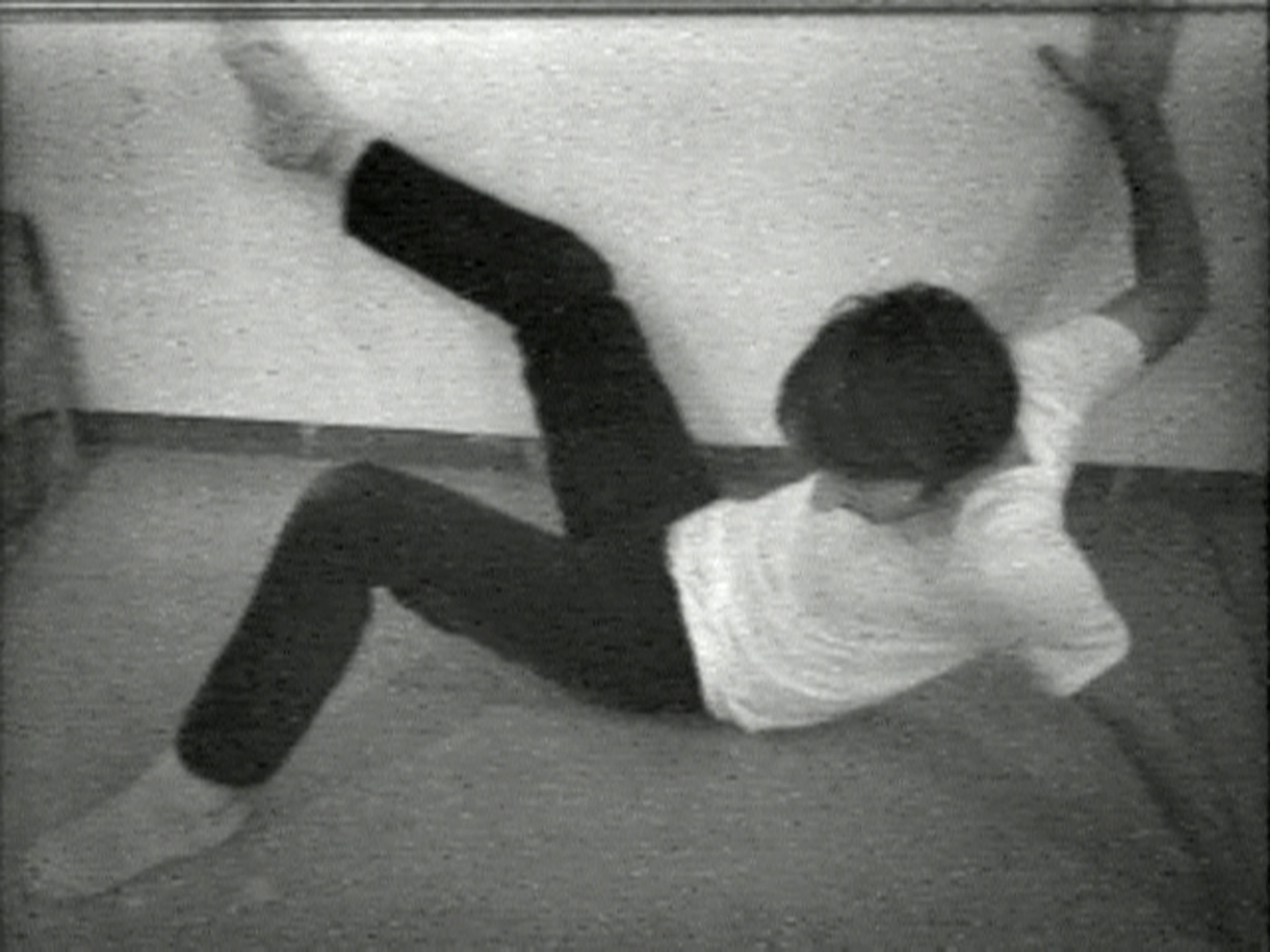 A grainy black and white image capturing a person in mid-fall or stumble, with their arms flailing and legs in an awkward position, suggesting motion and imbalance.