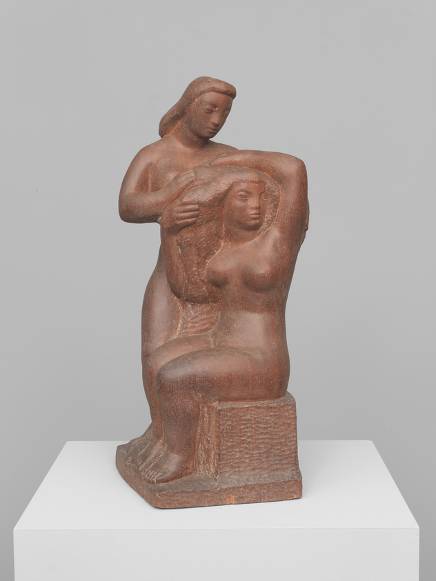 A terracotta sculpture depicting two stylized female figures, one standing and one seated, with the standing figure gently resting her hand on the seated figure's shoulder. The figures are presented on a white pedestal against a neutral background.