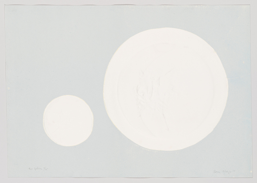 A light blue paper background with two embossed circular shapes, one significantly larger than the other, with faint, intricate designs visible upon closer inspection. The smaller circle is on the left and the larger one is on the right. There is handwritten text at the bottom left corner and a signature with a date '87 at the bottom right corner.