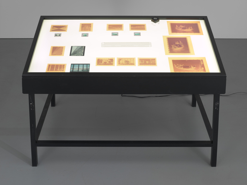 A light table displaying various photographic negatives and slides, arranged in a grid pattern, with a magnifying tool on the top right corner.