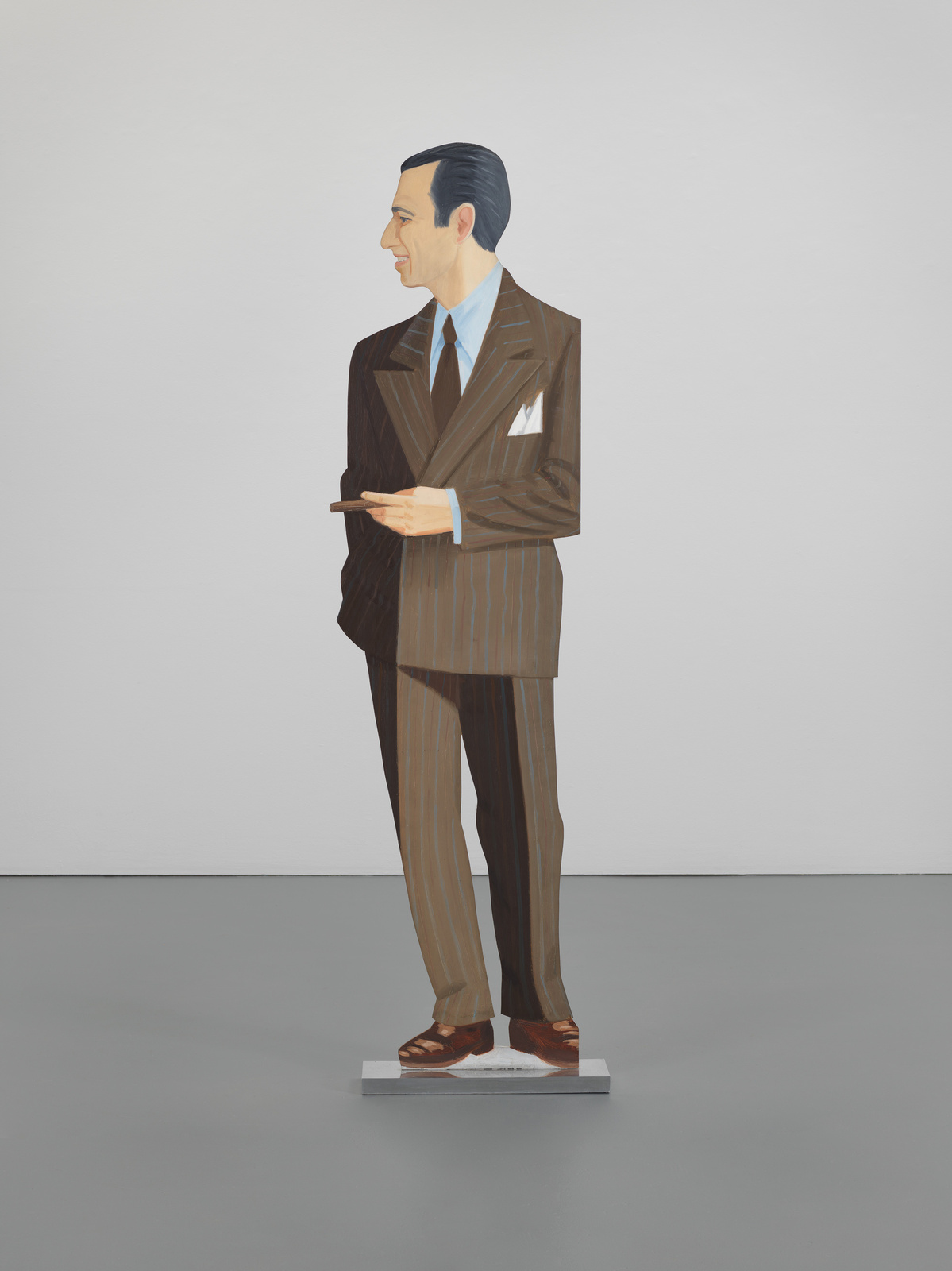 A painting of a stylized man standing in a gallery space, depicted in a brown pinstripe suit with a blue shirt and a light pocket square. The figure has slicked-back dark hair, a pronounced chin, and a slight smile, with one hand extended as if gesturing during a conversation. The artwork has a three-dimensional appearance with the figure standing on a small white platform, giving the illusion of a real person in the space.