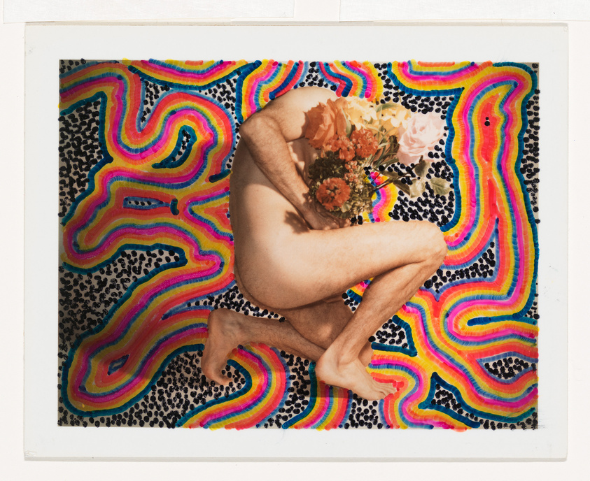 A photograph of a person in a fetal position on a psychedelic background with vibrant, wavy rainbow patterns and leopard spots. The person's head is replaced by a bouquet of flowers, obscuring their identity. The image has a white border, resembling a Polaroid.