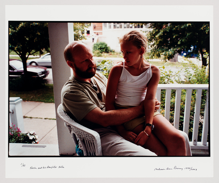 A man with a beard and a young girl sitting closely together on a white wicker chair on a porch, with a suburban street visible in the background. The man is looking at the girl, who is gazing away with a thoughtful expression. There is handwriting at the bottom of the image that reads "Kevin and his daughter Kate" and the artist's signature with the date.