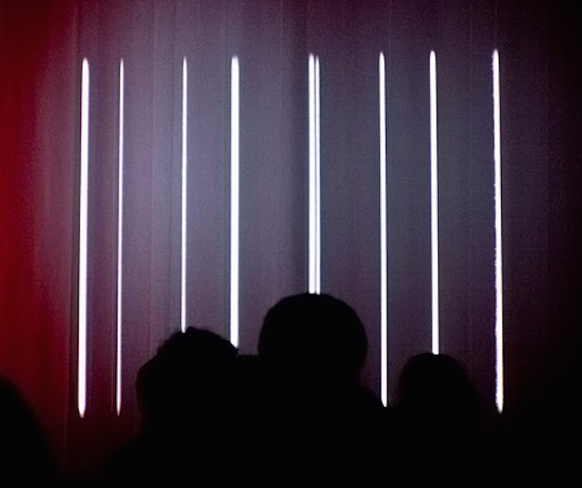 Silhouettes of people against a backdrop of vertical light beams on a stage.