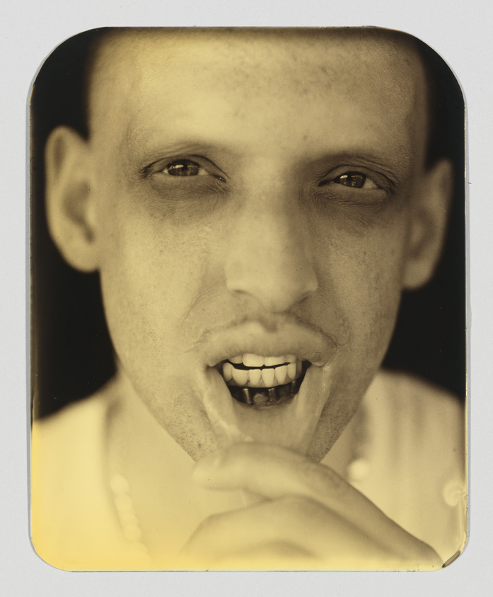 Close-up sepia-toned photograph of a man with a playful expression, biting his finger and smiling at the camera.