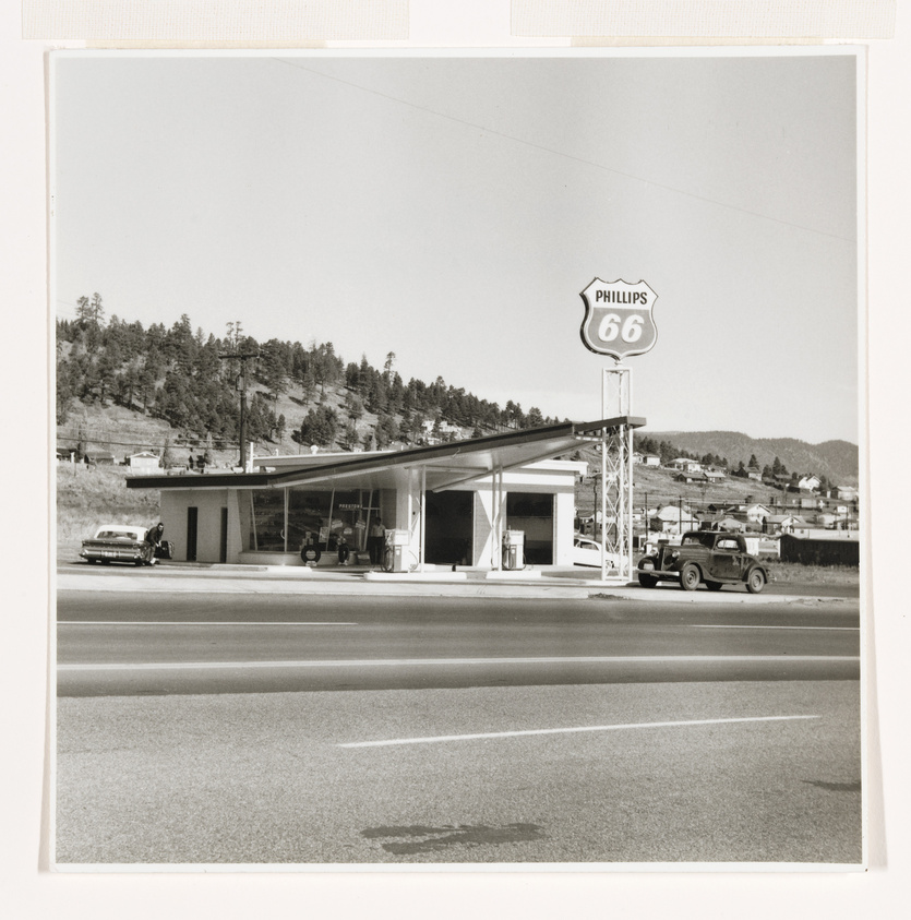 Vintage Phillips 66 gas station with cars, set against a backdrop of hills and clear skies.