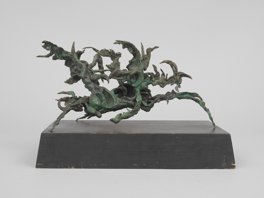 A complex, abstract bronze sculpture with dynamic, twisting forms and protrusions, mounted on a rectangular black base, against a neutral background.