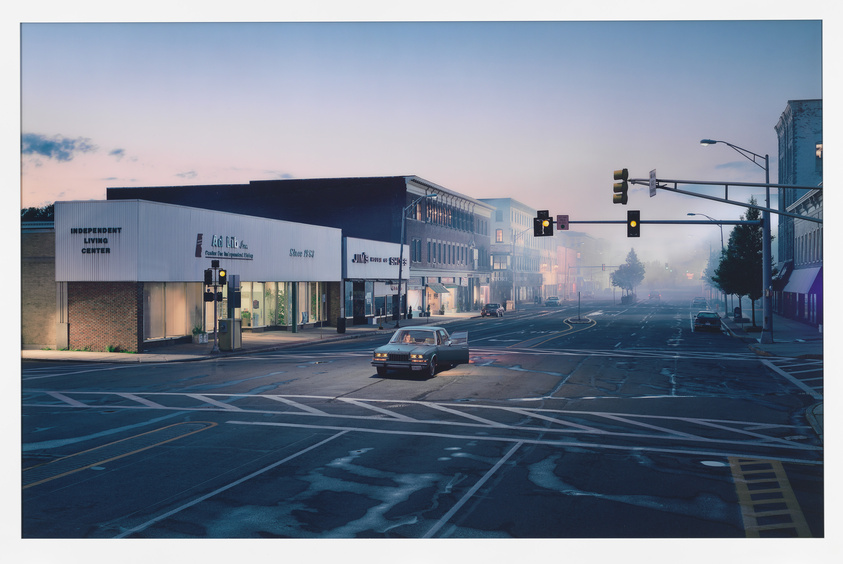 Early morning in a quiet town with mist, vintage car at a traffic light, and storefronts.
