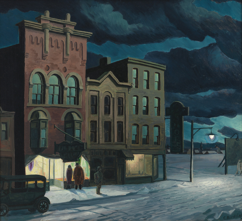 Street scene at night with people outside a lit storefront, under a cloudy sky.