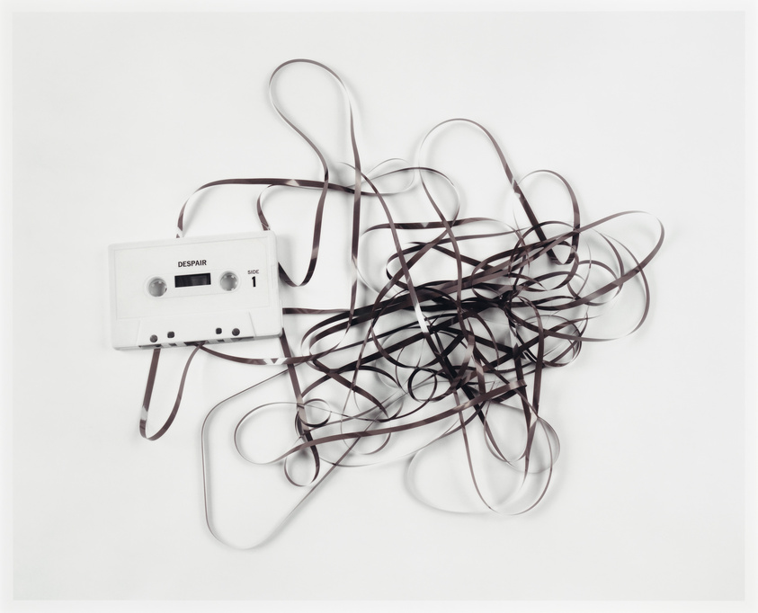 A tangled cassette tape with the word "DESPAIR" on its label, unraveled and spread out on a white surface.