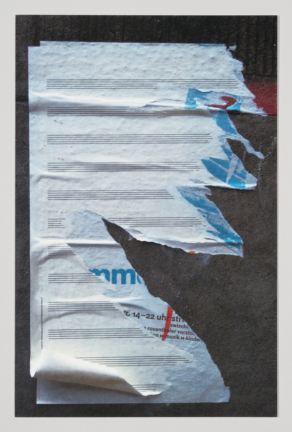 A weathered bulletin board with layers of torn paper posters, revealing partial text and images, suggesting a history of past events and advertisements. The background is a textured dark surface, and the remnants of the posters are primarily white with hints of blue and red graphics.