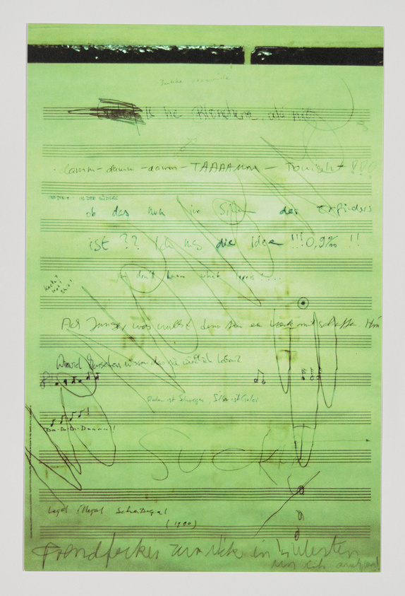 A photograph of a green-tinted paper filled with various handwritten notes, scribbles, and musical notations. The writing appears to be in German, with some words and phrases underlined or written in bold, and musical notes scattered throughout the text. The overall appearance is chaotic and resembles a brainstorming session or a composer's rough draft.