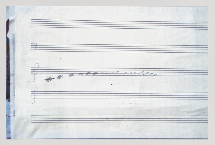 A photograph of a sheet of music paper with a few handwritten musical notes and symbols, including a treble clef and a key signature, on a stave with some visible creases and signs of wear.