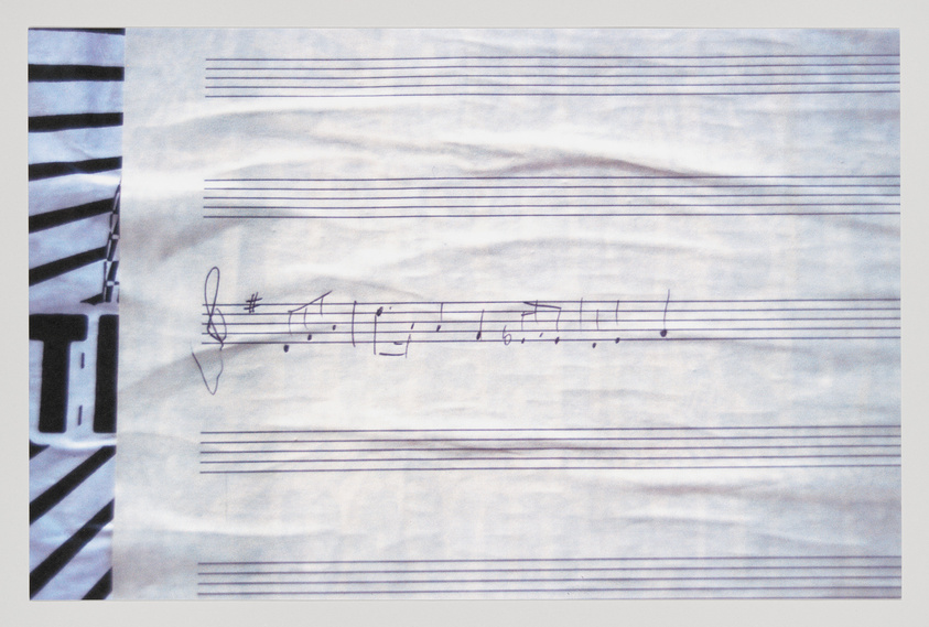 A photograph of a piece of paper with musical notation, including a treble clef and several notes on a staff, with the left edge of the paper slightly crumpled.