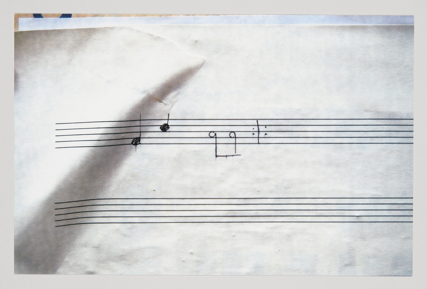 A photograph of a piece of paper with musical notation, showing a torn upper left corner and signs of wear. The staff lines are drawn by hand and contain a few musical notes and symbols, suggesting an unfinished composition or a musical idea in progress.