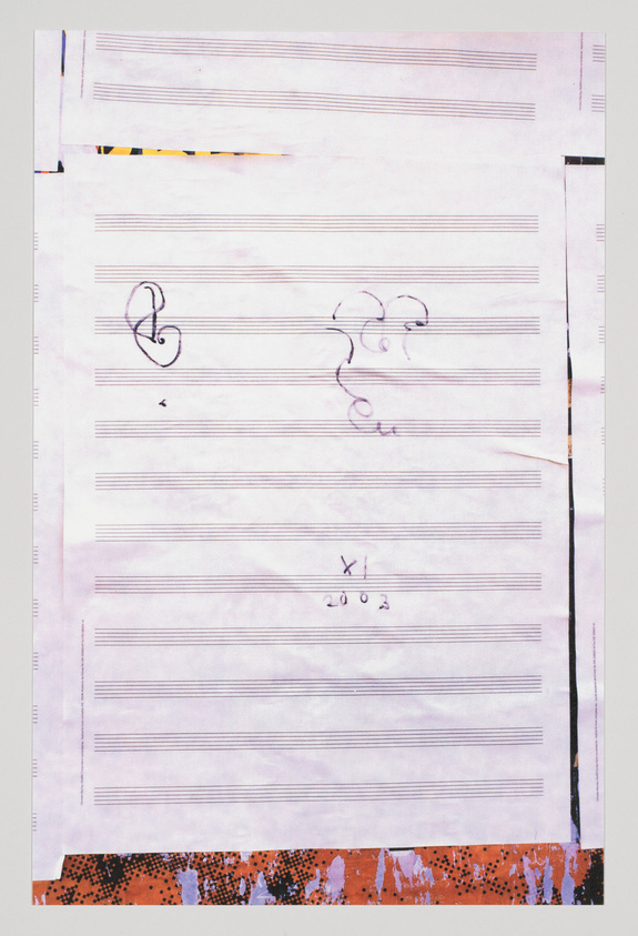 A photograph of a piece of paper with musical staff lines and a few musical symbols, including a treble clef and a bass clef, with some handwritten markings. The paper appears to be on a surface with a colorful, textured border at the bottom edge.
