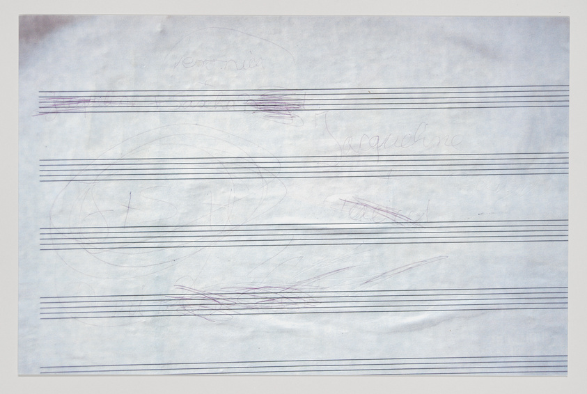 A piece of paper with musical staff lines and various scribbles and doodles in pen and pencil, including some cursive writing that is not fully legible.