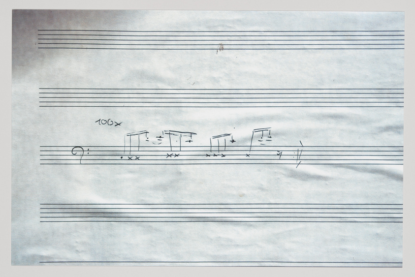 A photograph of a sheet of music paper with handwritten musical notation, including a clef, notes, and rests, with some annotations and symbols that appear to be instructions for the musician.