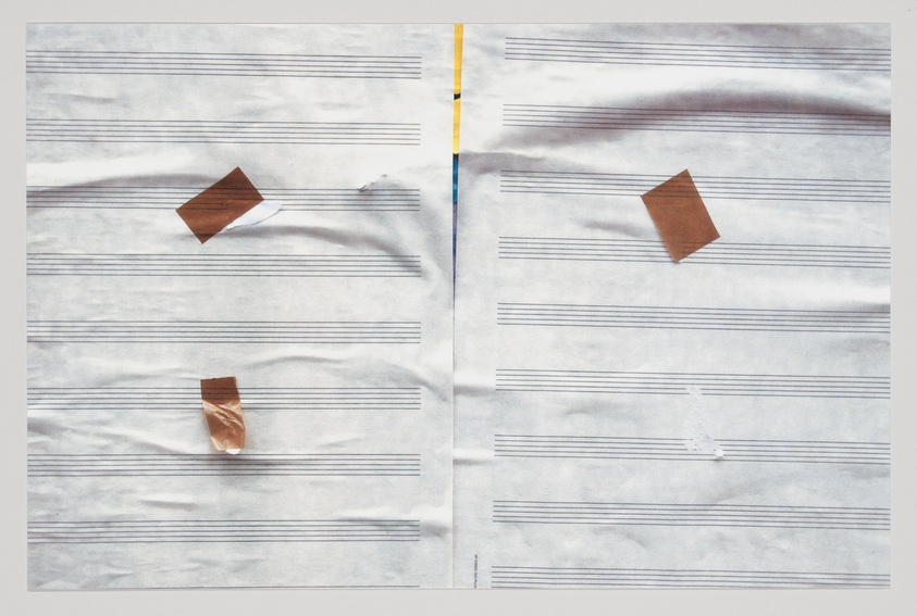 A crumpled piece of paper with printed music staff lines and three pieces of brown tape, two shaped like diamonds and one as a rectangle, placed to resemble notes on the lines. A vertical yellow and blue stripe runs down the center where the paper seems to be folded.