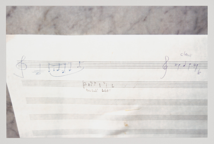 A worn piece of paper with musical notations scribbled on staves, including a treble clef and a few notes. There are handwritten annotations indicating "classic" and "Bartok Lbot!" on the right side, suggesting stylistic references or instructions for the music. The paper appears aged with some creases and stains.