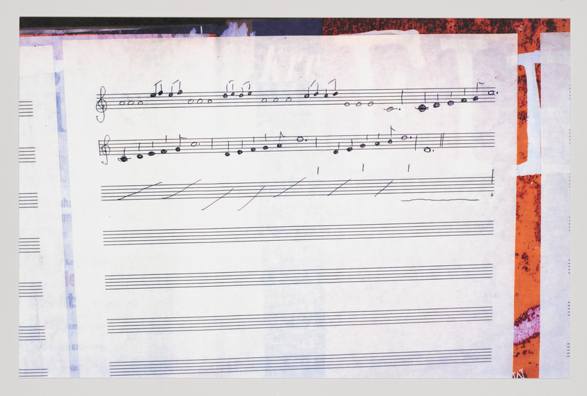 A photograph of a sheet of music paper with handwritten musical notation, including a treble clef and various notes and rests. The paper is surrounded by a collage of textured materials with red and purple hues. Some staves are filled with music while others are blank or partially filled.