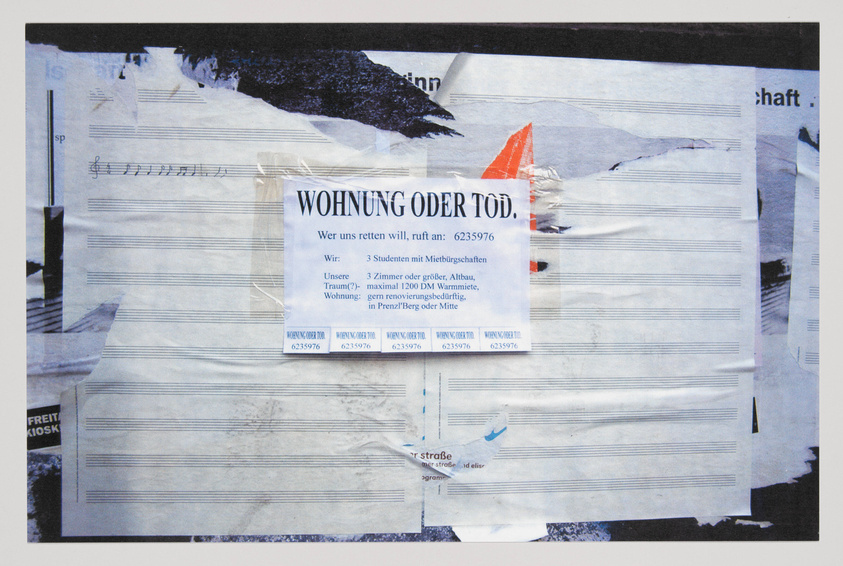 A collage of torn and layered papers with various texts, images, and musical notation, prominently featuring a central paper with the German words "WOHNUNG ODER TOD" (apartment or death) and a contact number. The background includes parts of a snowy landscape and other obscured print material.